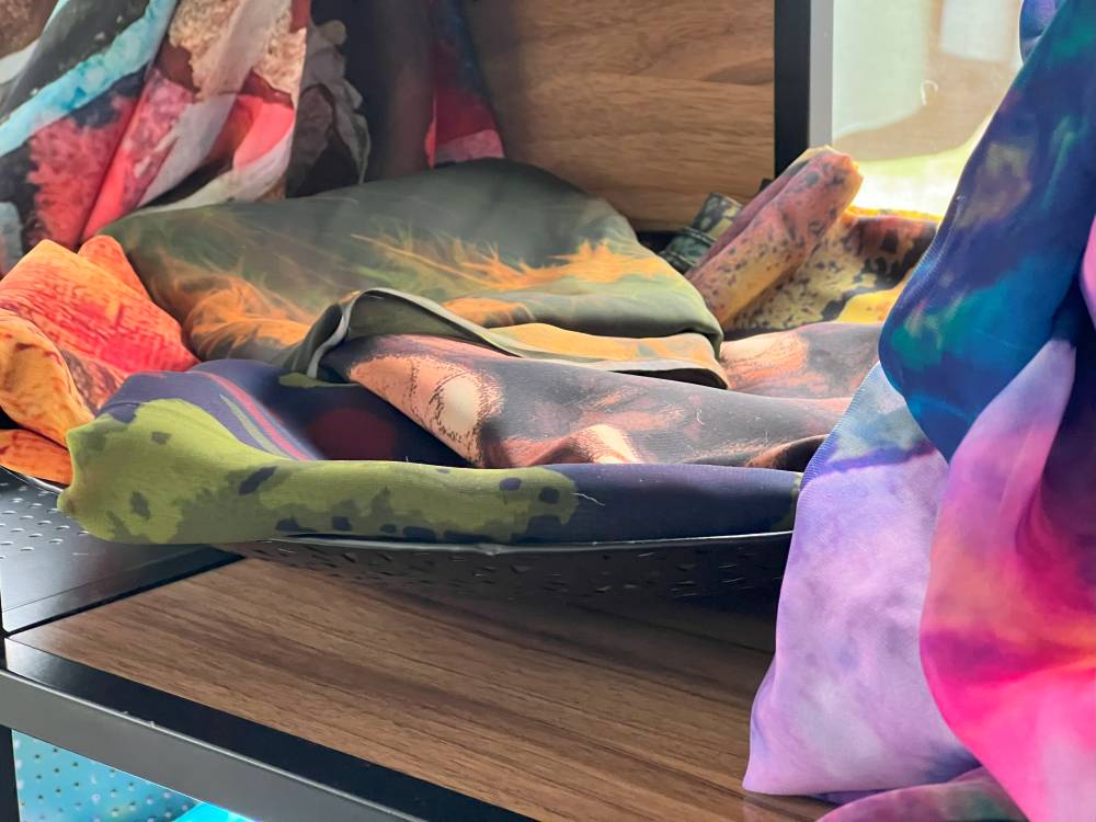 Photograph: two scarves draped over a mannequin and five scarves folded on a shelf. A range of colours and designs are evident.